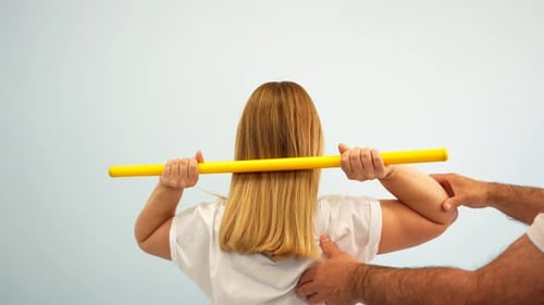 Physiotherapy patient doing shoulder mobility exercise with gymnastic stick. Medium shot, rear view