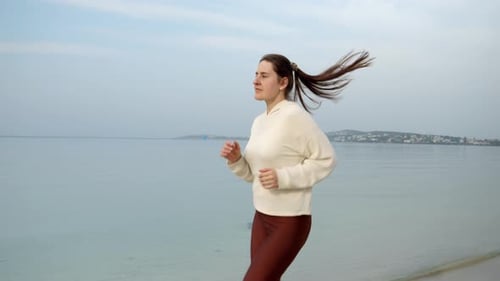 Slow motion of young woman staying fit and active by running on the sandy sea beach