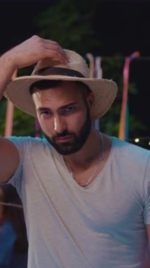 Man Adjusts Straw Hat at Night