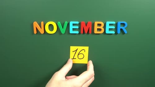 Hand sticking a sticker 16 November calendar day on school board. 16 date of November. Sixteenth