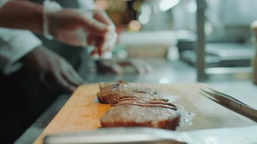 Chef Seasoning Sliced Steak in Commercial Kitchen