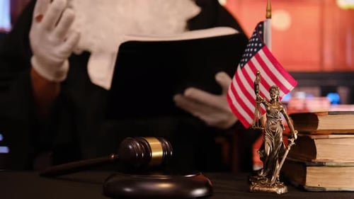 Judge in Robe Reviewing a Document at a Desk with a Gavel Law Books Justice Statue and American Flag