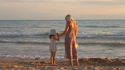 Back View of Mother and Daughter Look at Sea on Beach at Sunset Summer Vacation