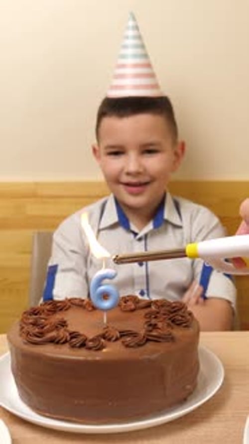05. The boy is sitting in front of a table with a festive cake, in which a candle in the form of the
