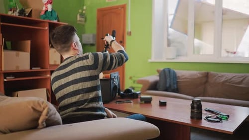 Man Arranges Camera Gear on Table in Home Studio Adjusting Lens and Microphone
