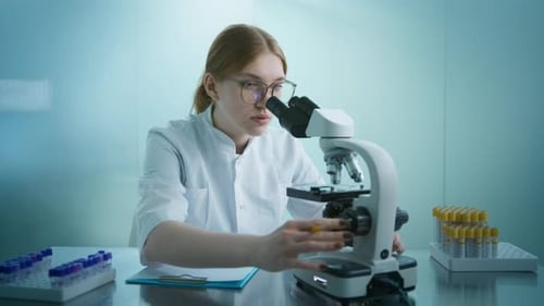 Woman Using Microscope and Taking Notes in Lab