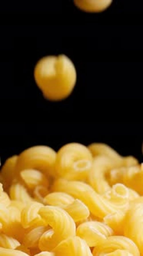 Raw macaroni pasta falls gracefully in stunning slow motion.