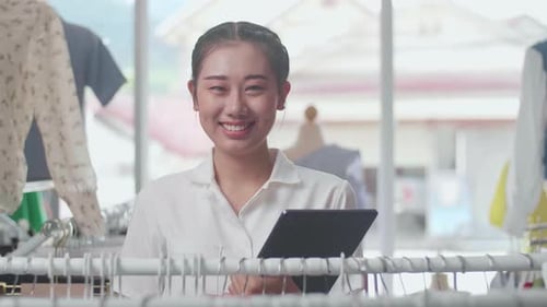 Close Up Of Asian Female Owner Of Clothing Store Smiling To The Camera While Using Digital Tablet