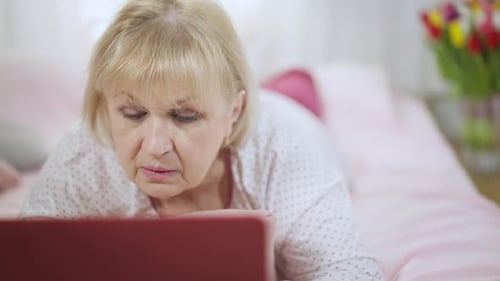 Senior Woman Lying on Bed Using Laptop
