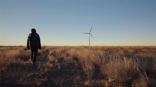Persona caminando por el campo hacia una turbina eólica distante