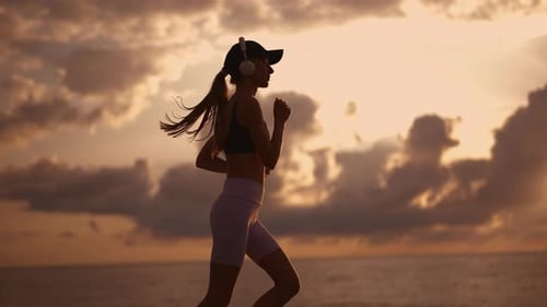 A Young Sporty Woman Runner is Listening to Music in Earphones and Training Workout Slim Fitness