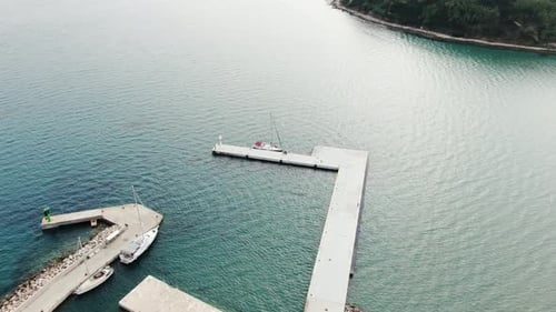 A drone shot of a lone sailing boat being docked on a stone pier. Flying closer and over the boat. T