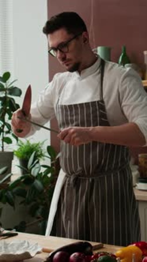 Vertical of Male Chef Sharpening Knife with Musat at Kitchen