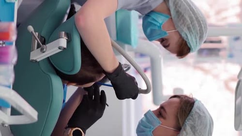 Two Woman Doctors in Medical Cap in Dental Clinic Serve the Patient Little Boy