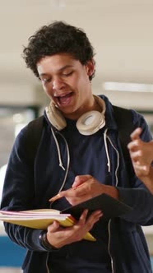 Vertical video: Watching peer gesturing student taking notes in hall with yellow notebook metal pen
