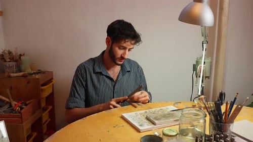 Craftsman working at a wooden table in a well-lit studio, shaving down wooden peices.