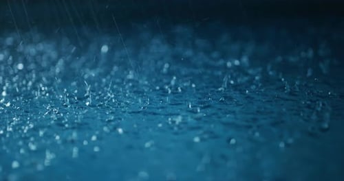 Cinematic macro shot of water drops falling down and splashing away in a sea or lake while raining