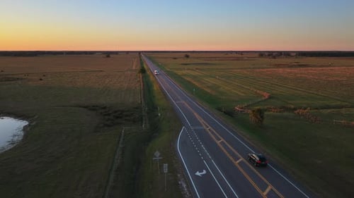 Aerial View of Rural Highway at Sunset with Cars Driving Fast Along a Straight Asphalt Road with