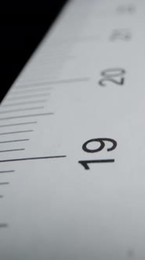 Vidéo verticale. Règle en papier sur fond noir, avec mesures centimétriques. Slider Dolly