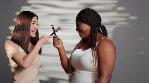 Joyful Young Women with Makeup Brushes Posing Indoors