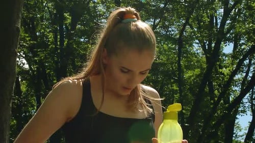 Athletic woman opens water bottle in sunny park