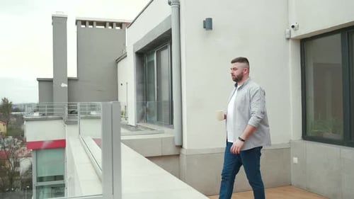 young handsome bearded man standing on modern balcony or terrace enjoying city view on urban