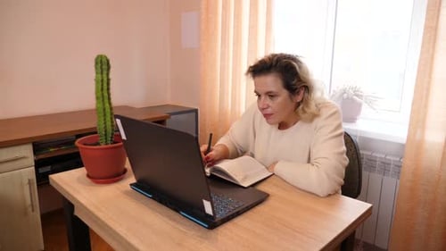 65. A woman sits at a table and works on a laptop at home.