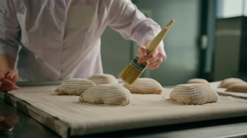 konzentrierte hübsche Bäckerin schmiert rohe Brötchen mit Ei vor dem Backen Backwarenherstellung