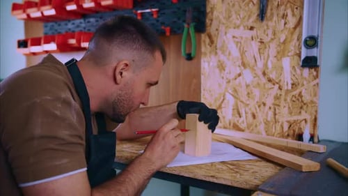 Schreiner skizziert auf Bauplan mit Holzblock in der Werkstatt