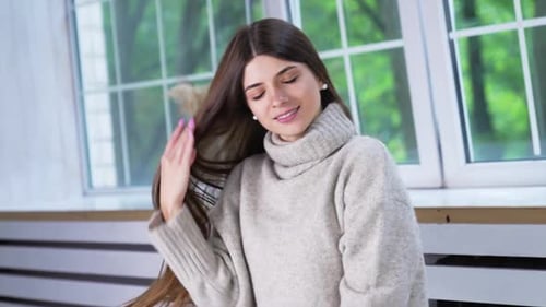 Attractive brunette in warm sweater indoors. Young lady touching her hair