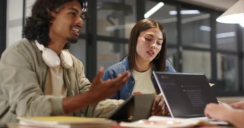 Homme d'équipe diversifié menant une conversation et faisant des gestes, une femme écoutant cherchant un accord avec un ordinateur portable à table