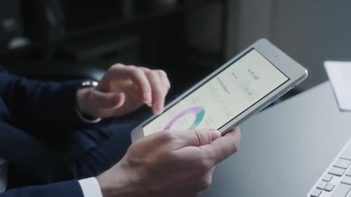 Hände eines Finanzanalysten untersucht Datendiagramme auf einem digitalen Tablet