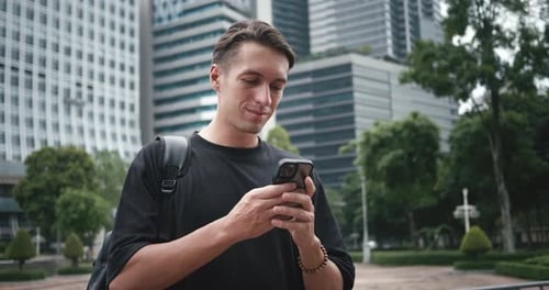 Smiling Man Student with Backpack Using Smartphone at City Street Male Student Tourist Browsing
