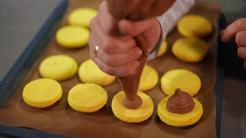 Nahaufnahme Quetschen von Schokolade aus einer kulinarischen Spritze auf gelben französischen Makronen in Zeitlupe