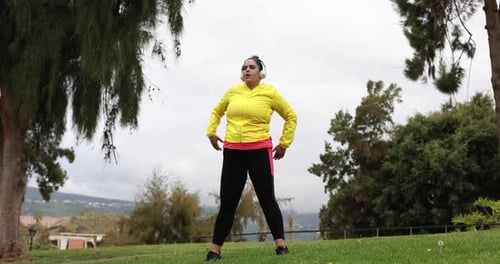 Woman Stretching in a Grassy Park with Headphones