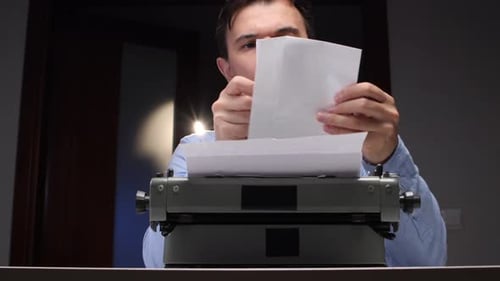 Man Examines Typed Letter at Vintage Typewriter Indoors