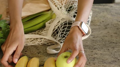 Las manos y los antebrazos extienden la bolsa de malla de la compra y crean una exhibición ordenada de plátanos y manzanas en el mostrador