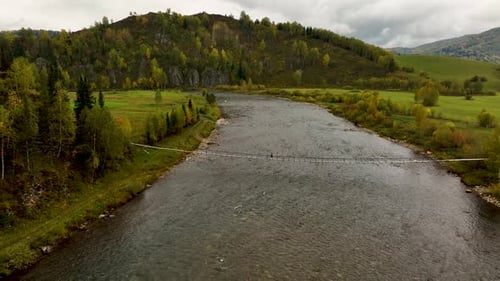 Person crossing a narrow suspension bridge over a wide river