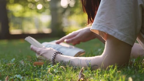 A young attractive girl lying on the green grass and reading a book