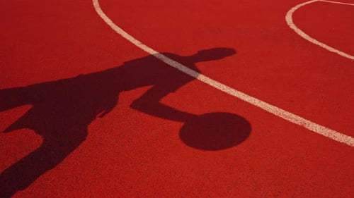 Close-up of a basketball guy's shadow on the floor of a basketball court while dribbling the ball