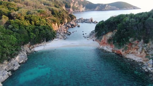 Aerial drone shot flying over turquoise water into a stunning, secluded white pebble beach