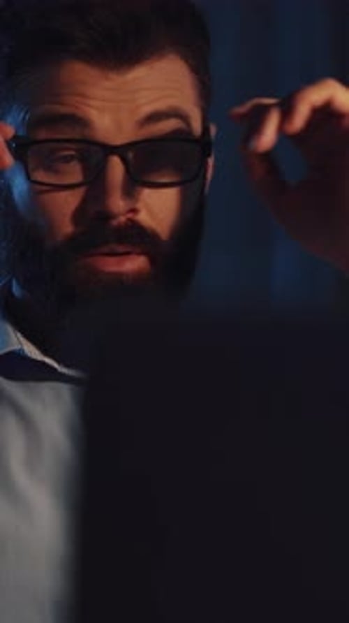 A Focused Man with Glasses Works Intensely on His Tablet and Computer