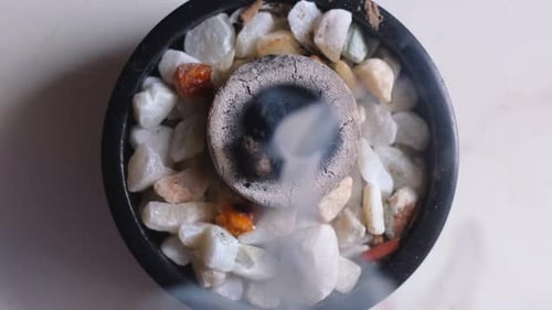 Close up top down view of burning incense with white smoke in a bowl with crystal gemstones, in 4K s
