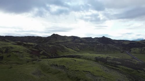 Slow Aerial push in on a mountainous lush volcanic landscape and rural road in central Iceland