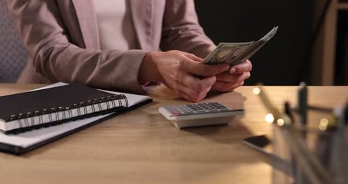 Woman Counting Cash at Desk with Calculator