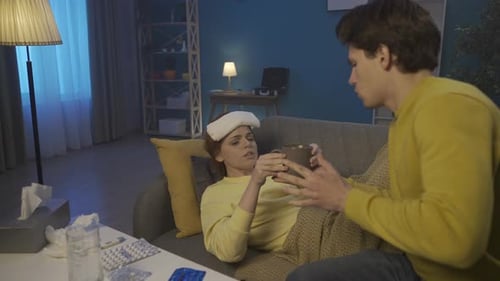 Un homme prend soin d'une femme lorsqu'elle est malade Une femme avec une compresse sur la tête est allongée sur le canapé a