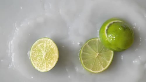 Sliced lime falling into white liquid water. Filmed in slowmotion.