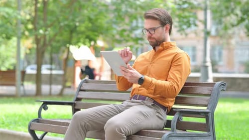 Man Surprised by Tablet News on Park Bench