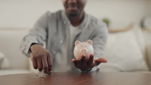 Investor spart Geld im Sparschwein Mann steckt Münzen in Spardose Nahaufnahme Junger Afroamerikaner