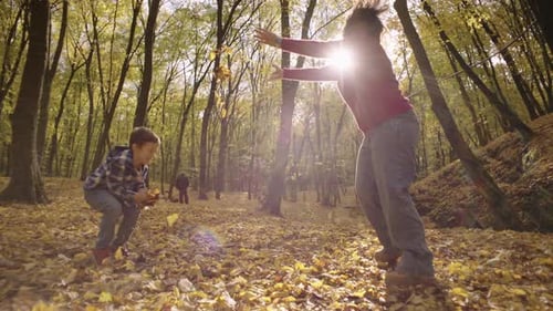 Boy and Woman Playing with Leaves in Autumn Forest